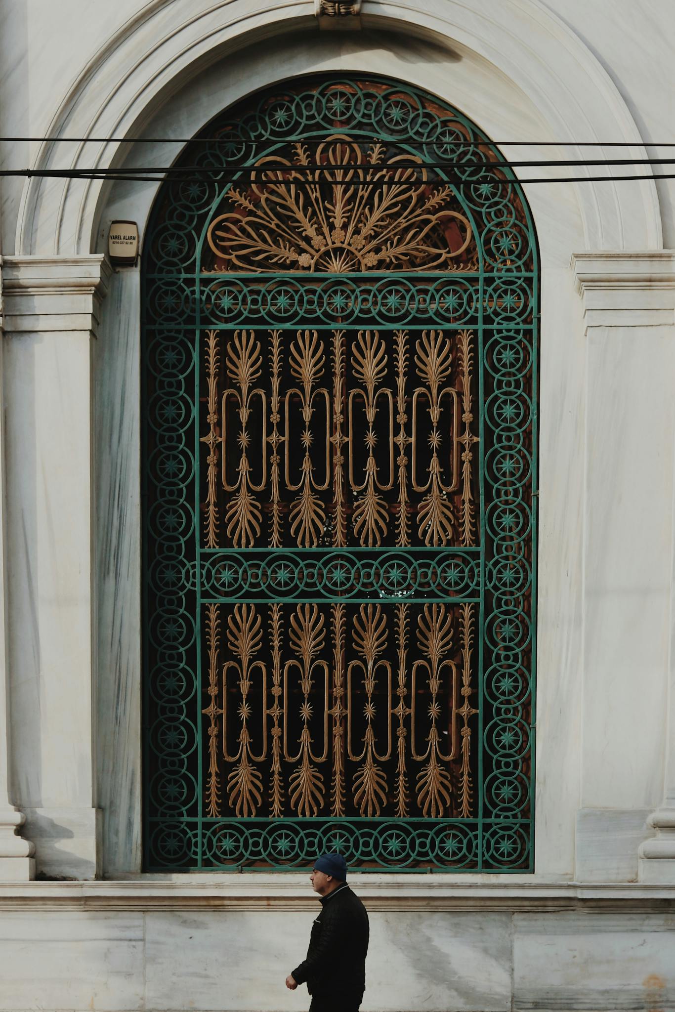 Side view of male passing by ornamental arched window with authentic oriental decor and metal bars